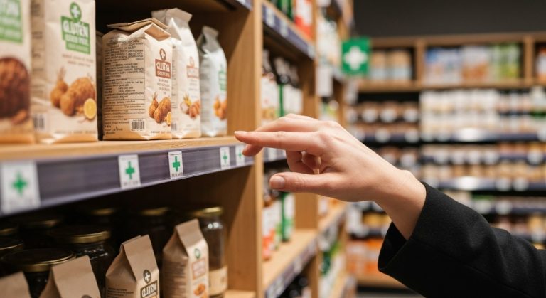 Ruka sahající po bezlepkové mouce v regálu obchodu se zeleným křížkem