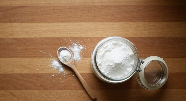 Skleněná dóza s kukuřičným škrobem na dřevěném kuchyňském stole s dřevěnou lžičkou