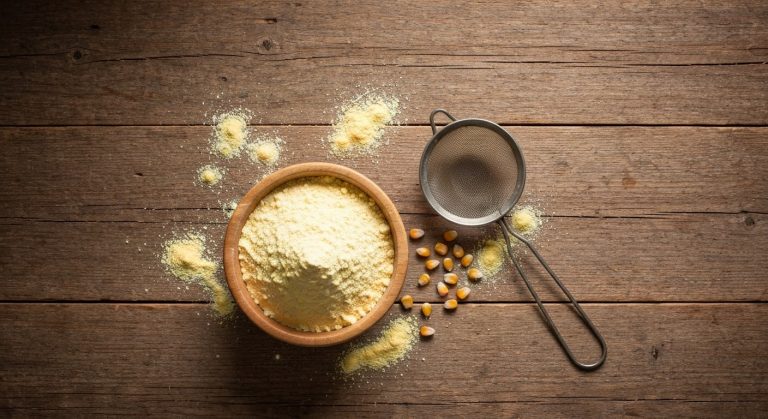 Jemná kukuřičná mouka v dřevěné misce na rustikálním stole s kovovým sítkem