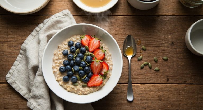 Miska bezlepkové ovesné kaše s čerstvými borůvkami a jahodami na dřevěném stole
