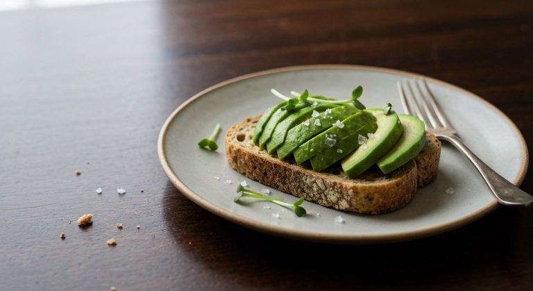 Detailní záběr na bezlepkový avokádový toast na keramickém talíři s drobečky na rustikálním dřevěném stole.