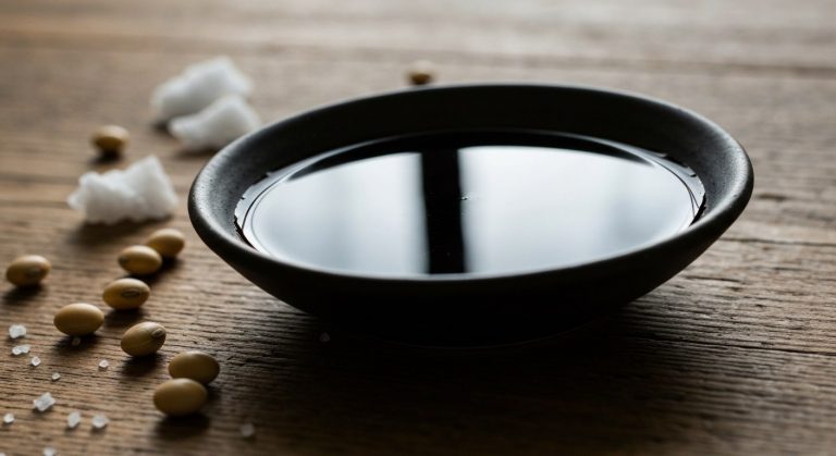 Nejlepší sojová omáčka bez lepku: Jak vybrat a nenaletět 9 Detailní záběr na tmavou keramickou misku se sójovou omáčkou tamari na dřevěném stole se sušenými sójovými boby.